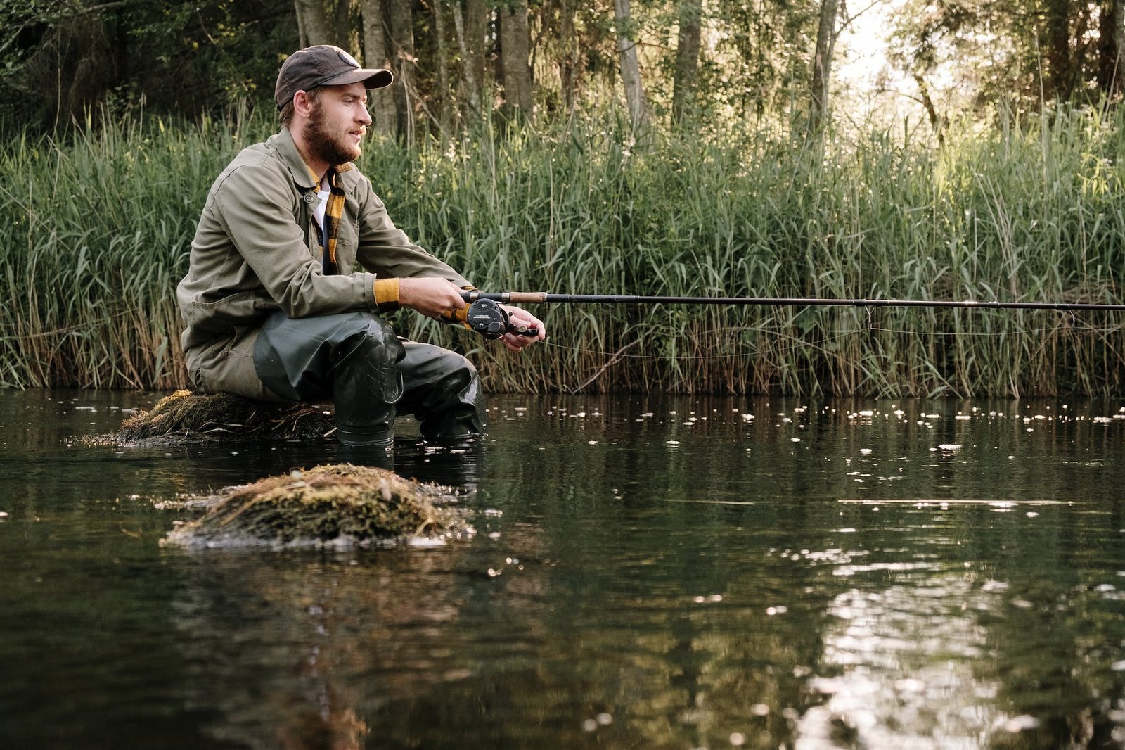 man in gray jacket and black pants sitting on brown rock in the river